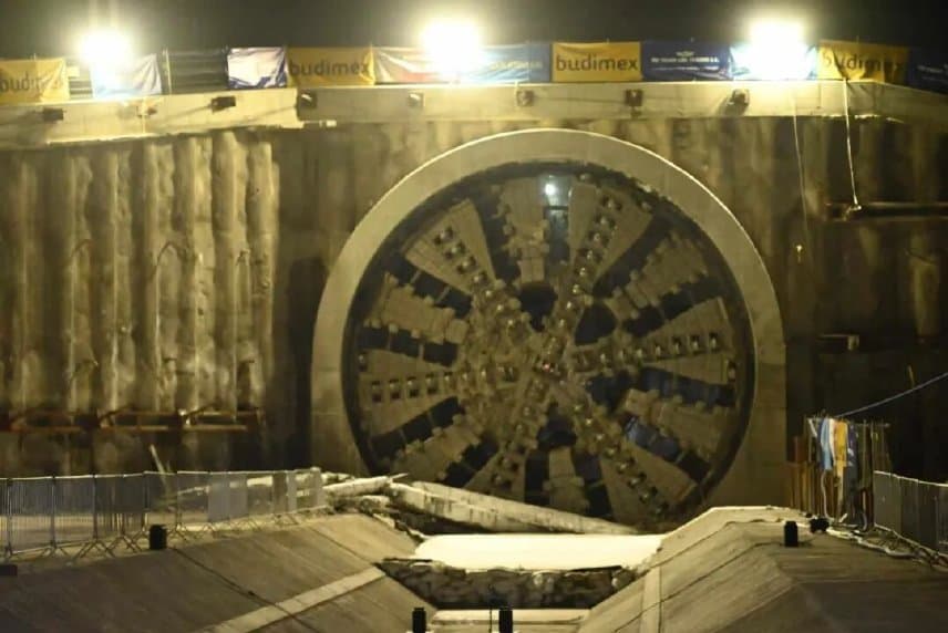 Head-on view of the TBM cutterhead emerging through the diaphragm wall at the breakthrough reception pit under the launch-area lighting