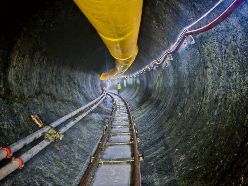 In-tunnel view along the bored hard-rock drive with ventilation duct, slurry lines and rail running back from the working face